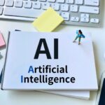 Card on a desk displays 'AI' with 'Artificial Intelligence' text, next to a keyboard and colorful sticky notes.
