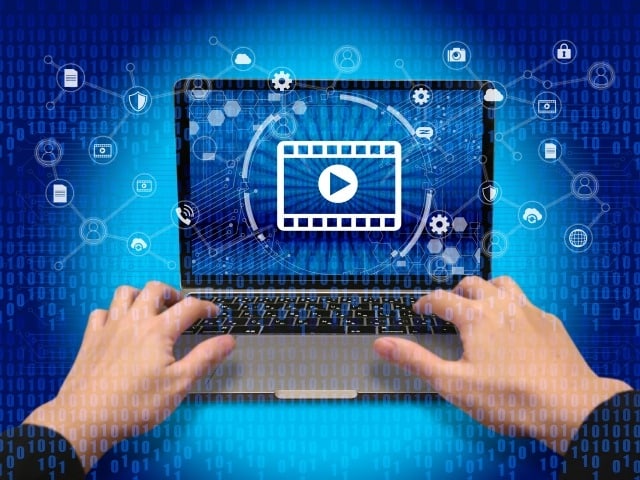 Hands typing on a laptop with a video play icon on the screen, surrounded by digital icons.
