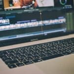 Laptop screen showing a video editing timeline with colorful clips; keyboard in foreground.
