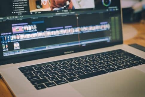 Laptop screen showing a video editing timeline with colorful clips; keyboard in foreground.