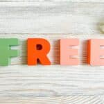 Green and orange letters spell 'FREE' on a light wooden surface with a small green plant in the corner.