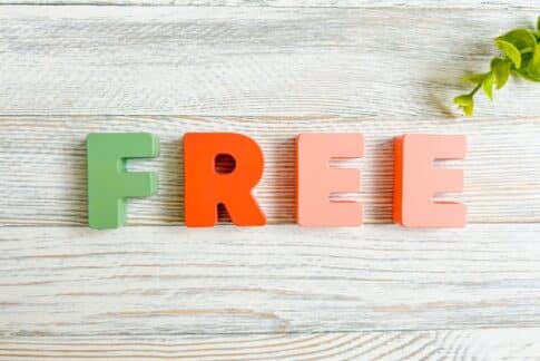 Green and orange letters spell 'FREE' on a light wooden surface with a small green plant in the corner.
