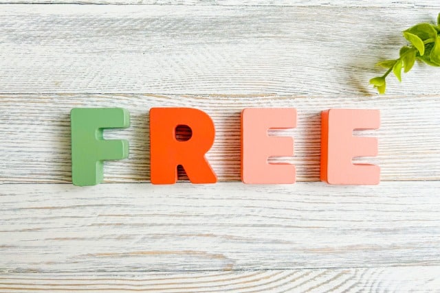 Green and orange letters spell 'FREE' on a light wooden surface with a small green plant in the corner.