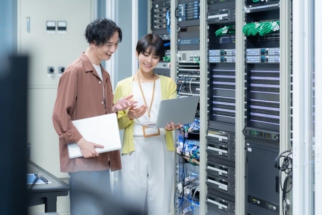 Two IT professionals review server rack hardware with a laptop in a data center, collaborating.