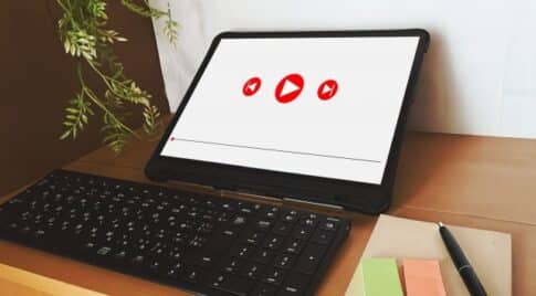 Tablet in landscape on a desk with a keyboard; screen shows three red play icons.
