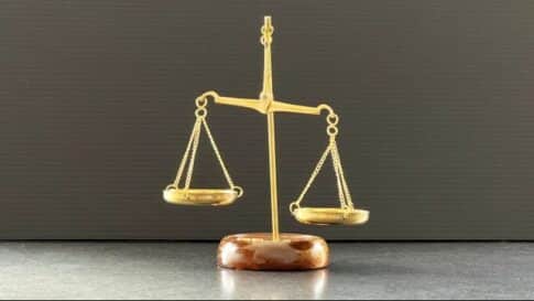 Gold balance scale on a wooden base, symbolizing justice or fairness, with weights balanced evenly against a dark backdrop.