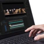 Close-up of a hand editing a video on a laptop, showing a timeline and preview window on the screen.