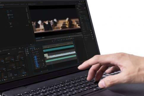 Close-up of a hand editing a video on a laptop, showing a timeline and preview window on the screen.