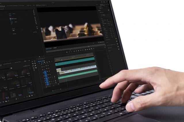 Close-up of a hand editing a video on a laptop, showing a timeline and preview window on the screen.