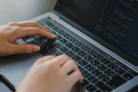 Close-up of hands typing on a laptop keyboard with code visible on the screen.