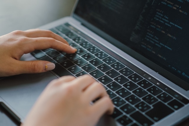 Close-up of hands typing on a laptop keyboard with code visible on the screen.