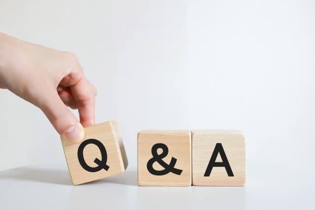 Hand placing a wooden block with the letter Q beside an ampersand and A spell 'Q & A' on a white surface.